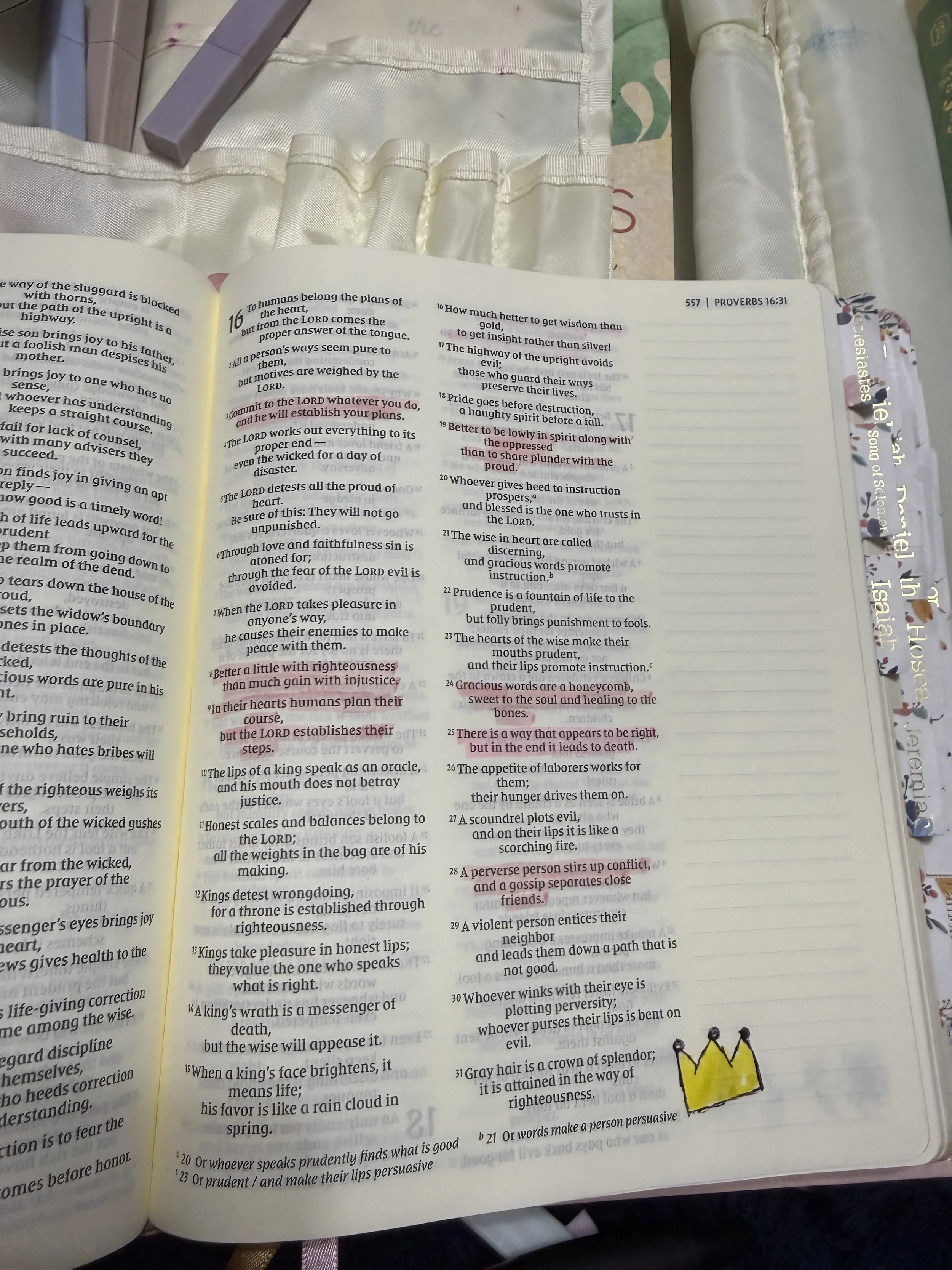 Open Bible opened to Proverbs 16:31 through 21:1, with a small yellow hand-drawn crown at the bottom right corner of the right page, on a satin cloth background.