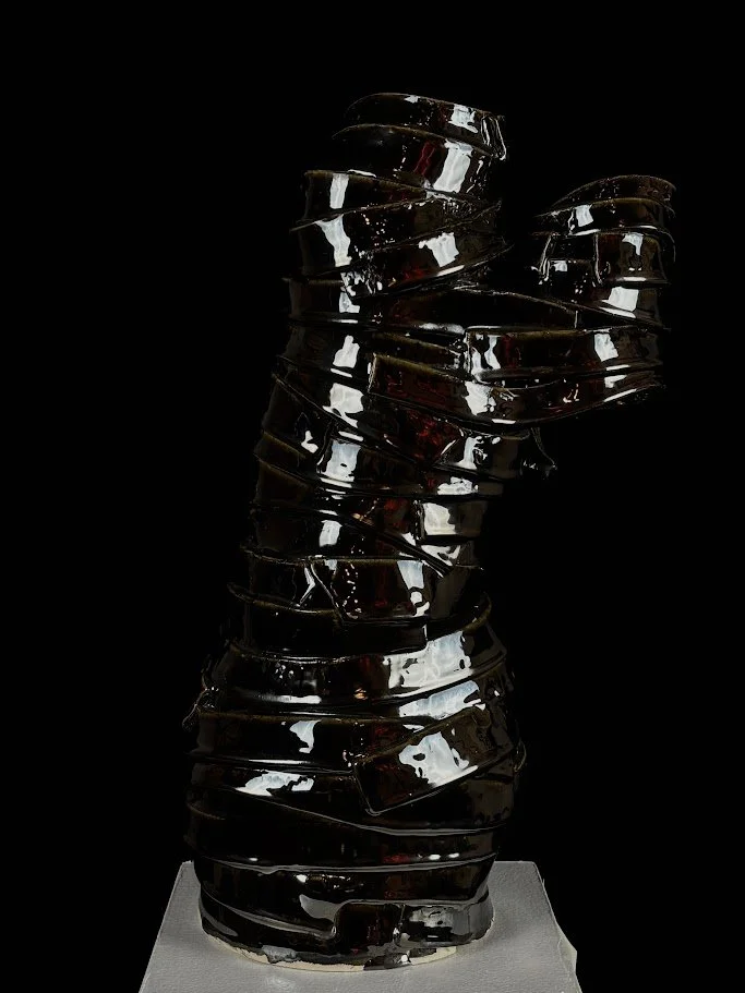 Sculpture made of stacked, irregularly shaped, dark glass pieces on a white base.