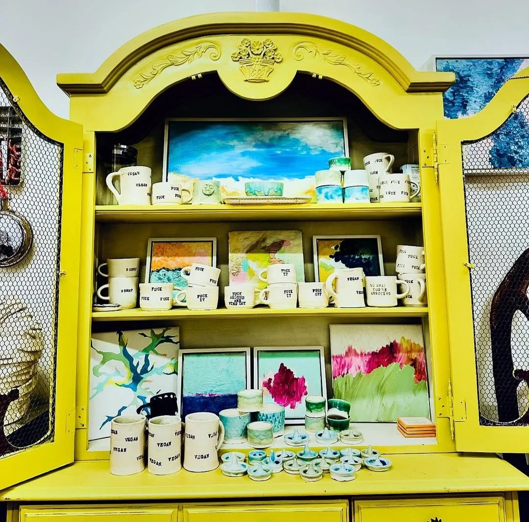 Yellow display cabinet showcasing various painted ceramics, mugs, and art pieces with colorful abstract and landscape designs.