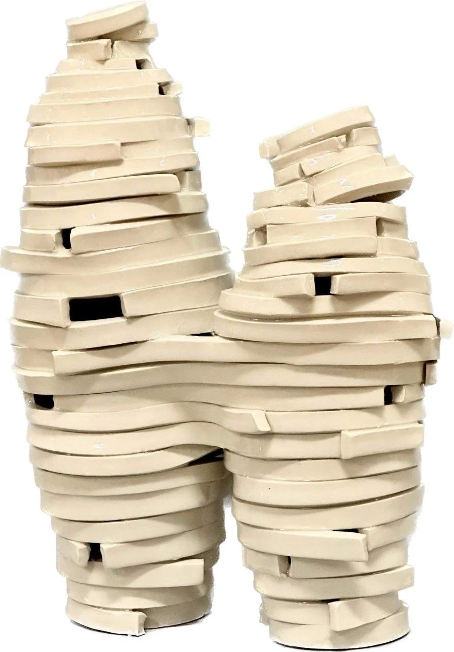 A sculpture made of stacked, unevenly arranged beige plastic or ceramic pieces resembling a human-like figure or animal with two legs and a rounded top.