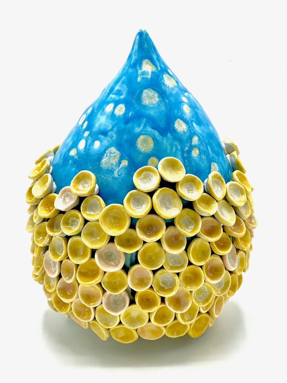 Decorative object resembling an egg, with a blue top section and a yellow bottom section covered with small yellow cup-like decorations.