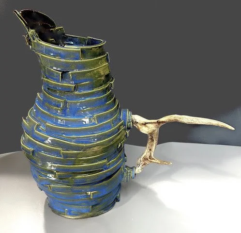 Ceramic vase with a blue and green glaze, featuring an unusual branch-like handle on the side.