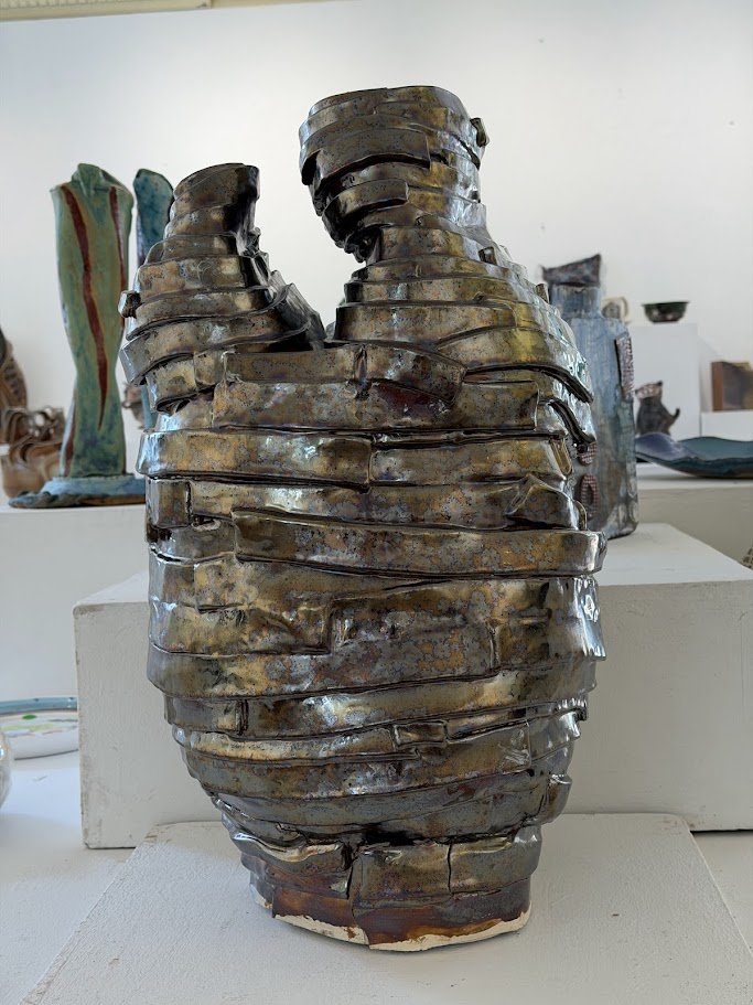 A ceramic sculpture resembling a human torso with interlocking horizontal bands, placed on a white pedestal in an art gallery.
