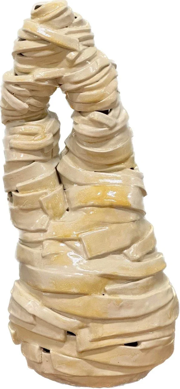 An abstract sculpture made of stacked, curved, cream-colored elements resembling thick, twisting ribbons or strips.