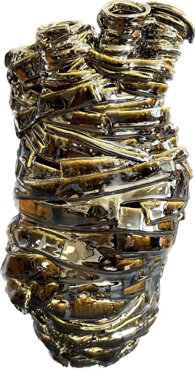 A close-up of a unique sculpture made of shiny, metallic, gold-colored material, resembling wrapped or folded fabric or metal strips.