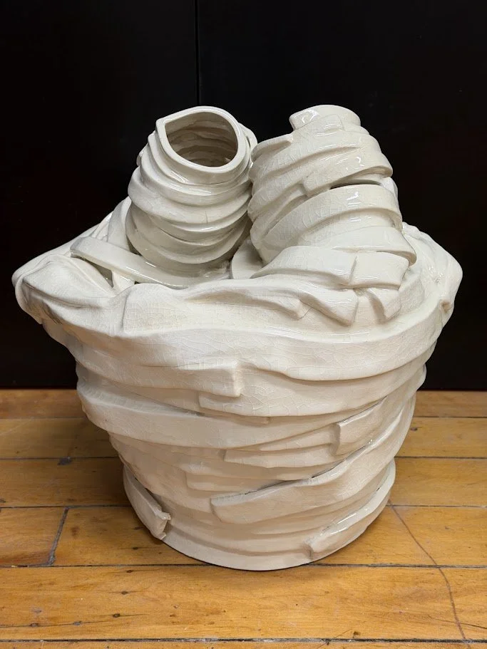 White ceramic or plaster sculpture resembling an overflowing basket of pita bread or tortillas on a wooden surface.