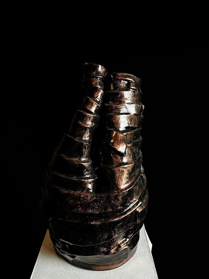 A dark metallic sculpture resembling a clenched fist on a white pedestal against a black background.