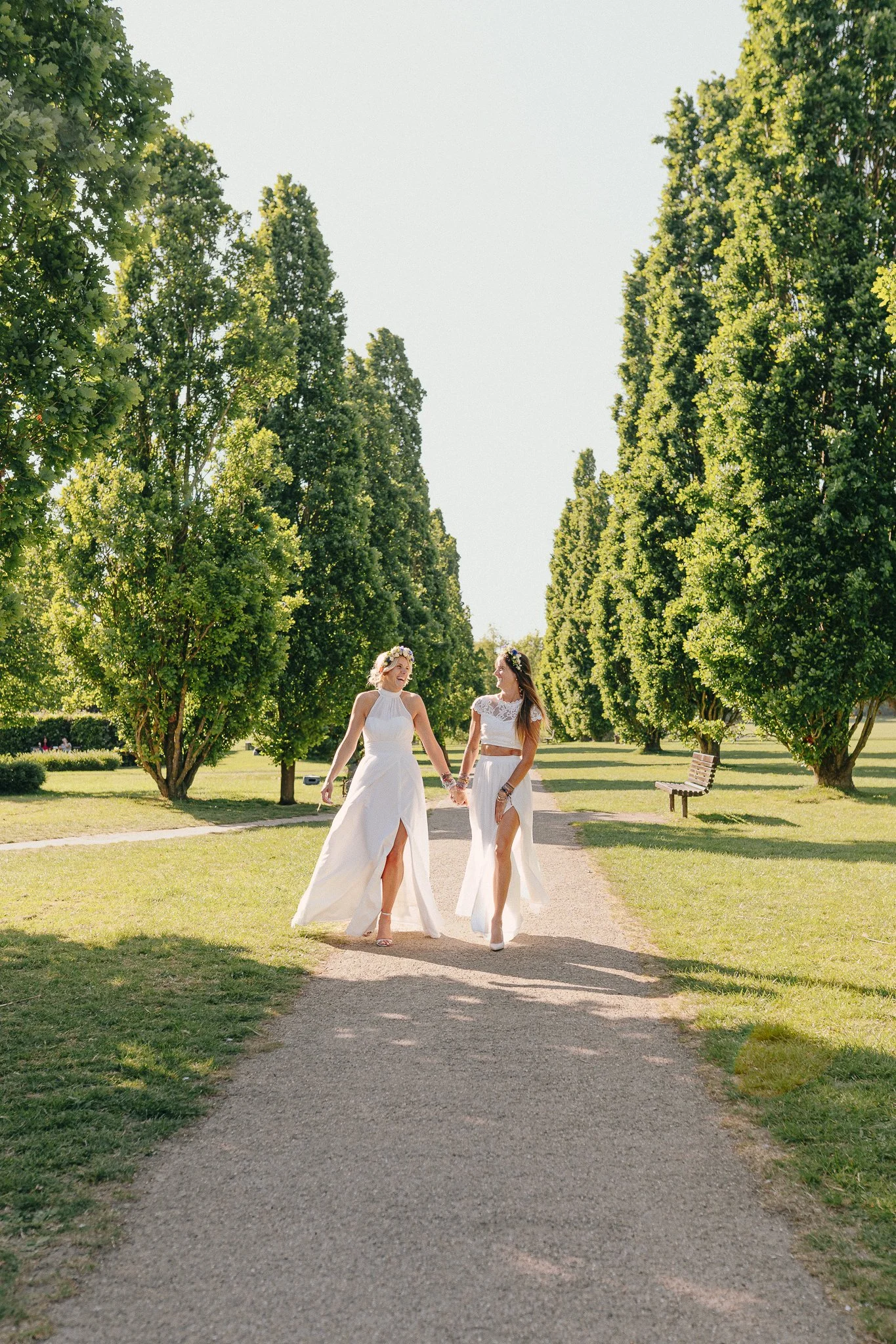 Two brides walking hand in hand between trees
