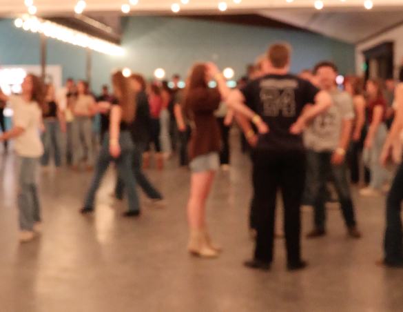 People dancing in a crowded room with string lights overhead.