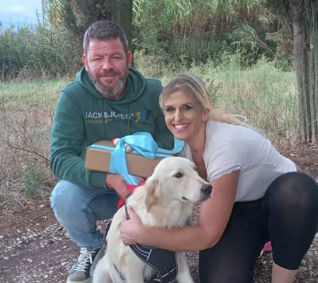 Due persone sorridenti con un cane da pastore, scattano una foto all'aperto in un'area boschiva