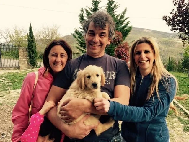 Tre persone sorridenti con un cane cucciolo in un giardino
