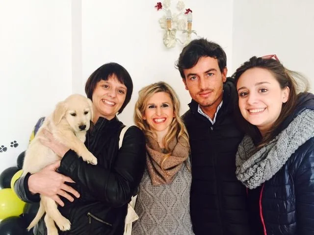 Cinque persone sorridenti in una stanza con un cane e decorazioni sulle pareti