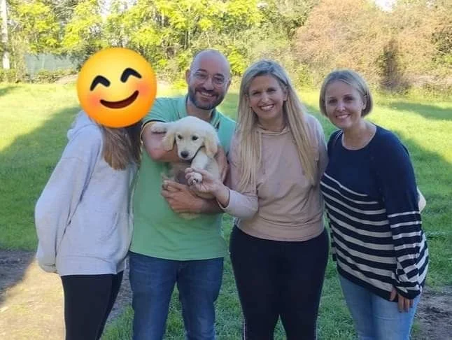 Quattro persone e un cane in un parco, con uno sfondo di alberi e cielo blu.