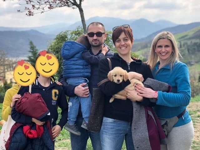 Gruppo di persone con un cane, in un paesaggio naturale con montagne sullo sfondo, durante una passeggiata.