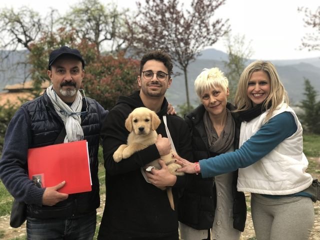 Quattro persone e un cucciolo di cane in un parco con alberi e montagne sullo sfondo.