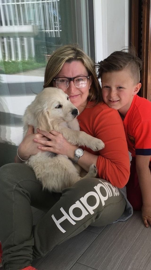 Donna, bambino e cucciolo di Golden Retriever sorridenti seduti su un pavimento in casa