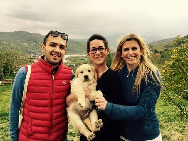 Tre persone sorridenti con un cucciolo di cane in un paesaggio di campagna montana