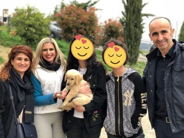 Gruppo di cinque persone con un cucciolo di cane, in un parco con alberi e foliage autunnale.