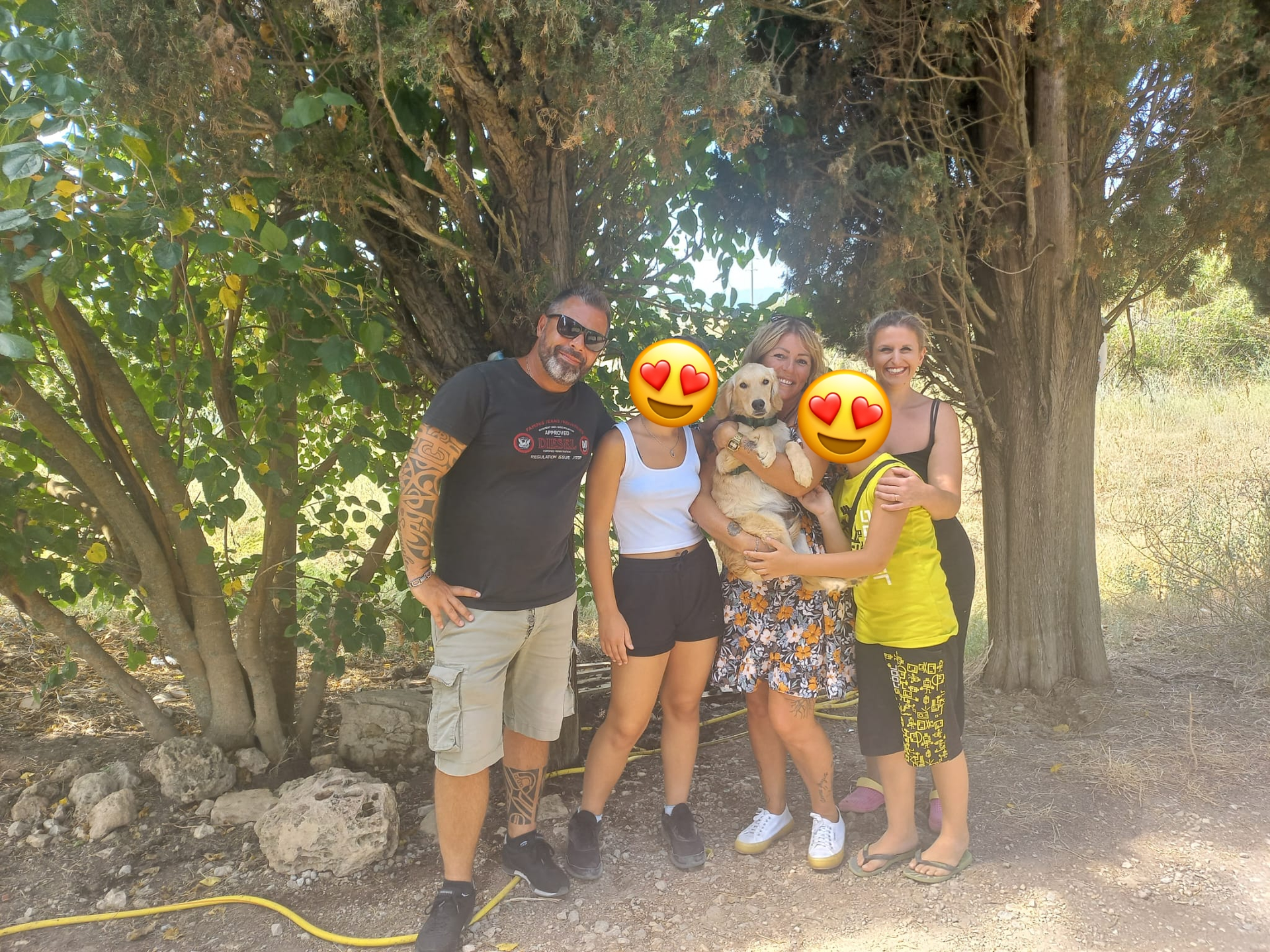 Gruppo di cinque persone sorridenti che posano sotto un albero, una con un cane, in un ambiente naturale soleggiato.