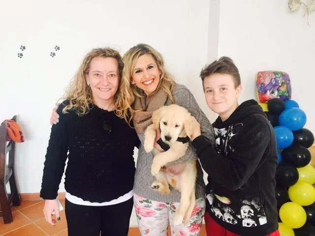 Due donne e un ragazzo tengono un cucciolo di cane in una stanza decorata con palloncini colorati.