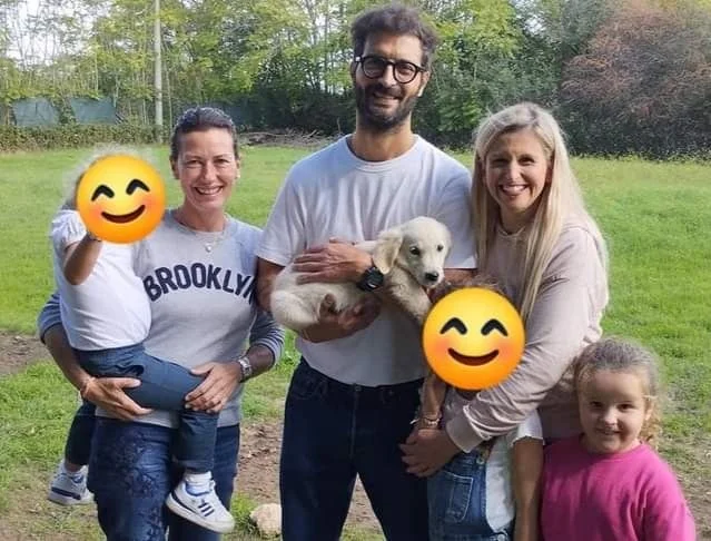 Gruppo di persone sorridenti con un cane, all'aperto in un parco, durante il giorno.
