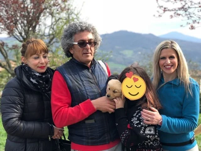Un gruppo di quattro persone e un cane, con un paesaggio naturale di colline e alberi sullo sfondo.