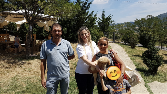 Tre persone in un giardino con un cane di pelo morbido e di colore chiaro, uno dei quali con un'icona sorridente che copre il volto.