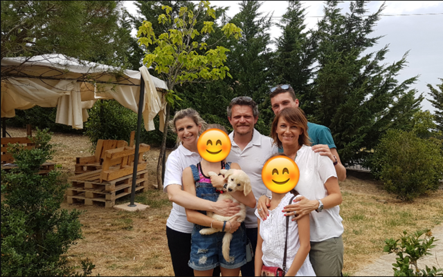 Una famiglia di sei persone e un cane in giardino, con alberi e una tenda in background.