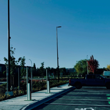Empty parking lot with charging stations, black pickup truck, and trees in the background.