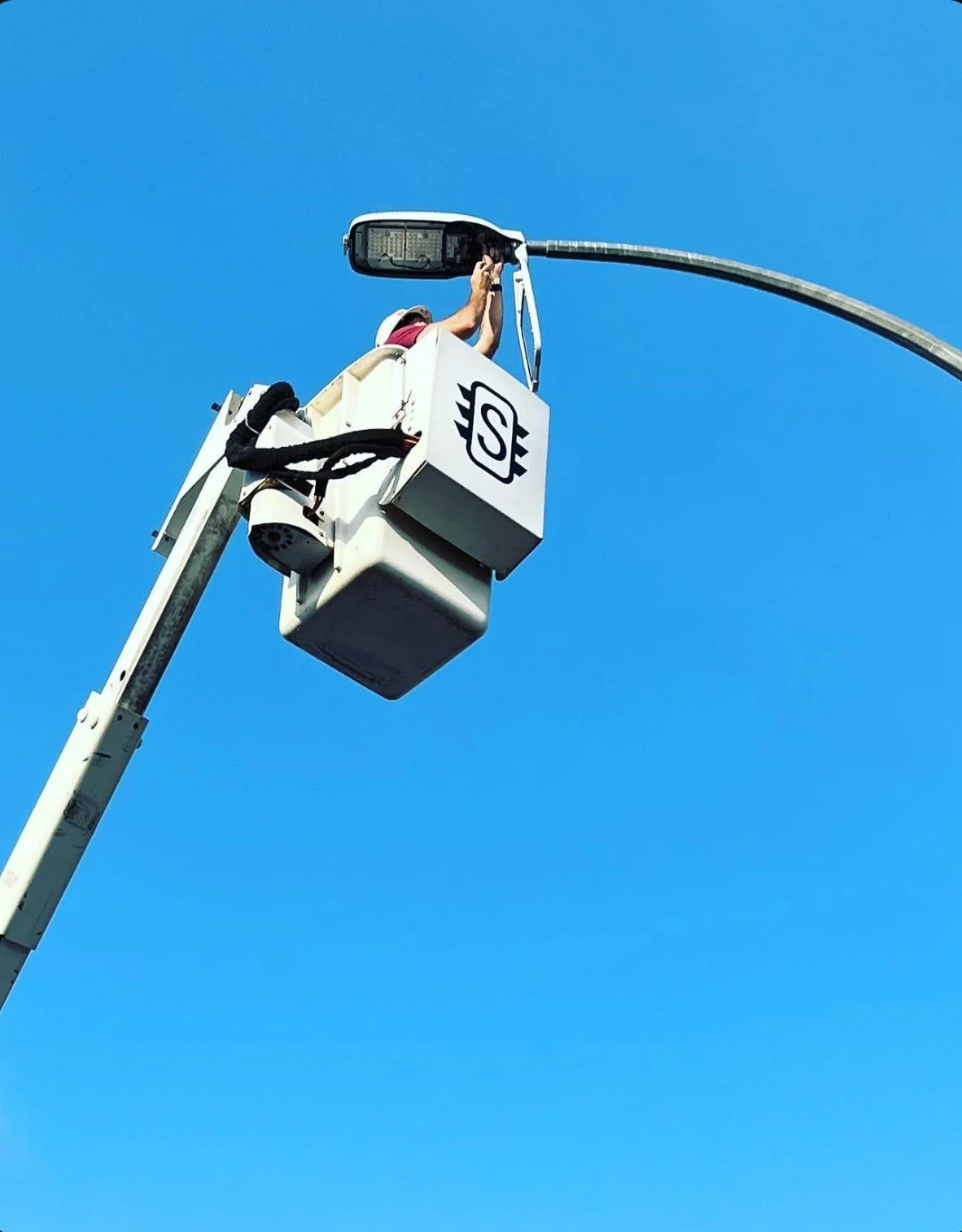 A worker in a cherry picker working on a streetlight against a clear blue sky.