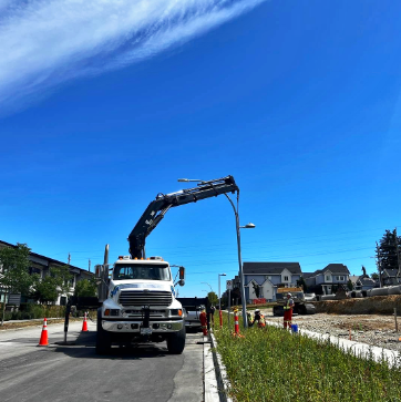 Street construction scene with a large truck and a crane lifting a streetlight over a residential neighborhood.