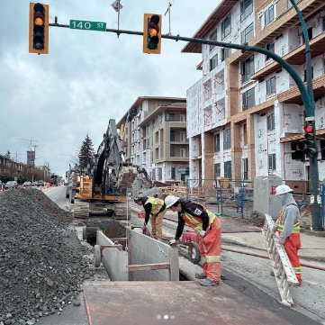 Construction workers working on a street, with a partially built building in the background and traffic lights overhead.