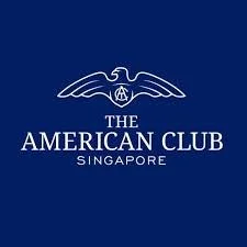 Logo of The American Club Singapore featuring a stylized eagle with outstretched wings above the club's name.