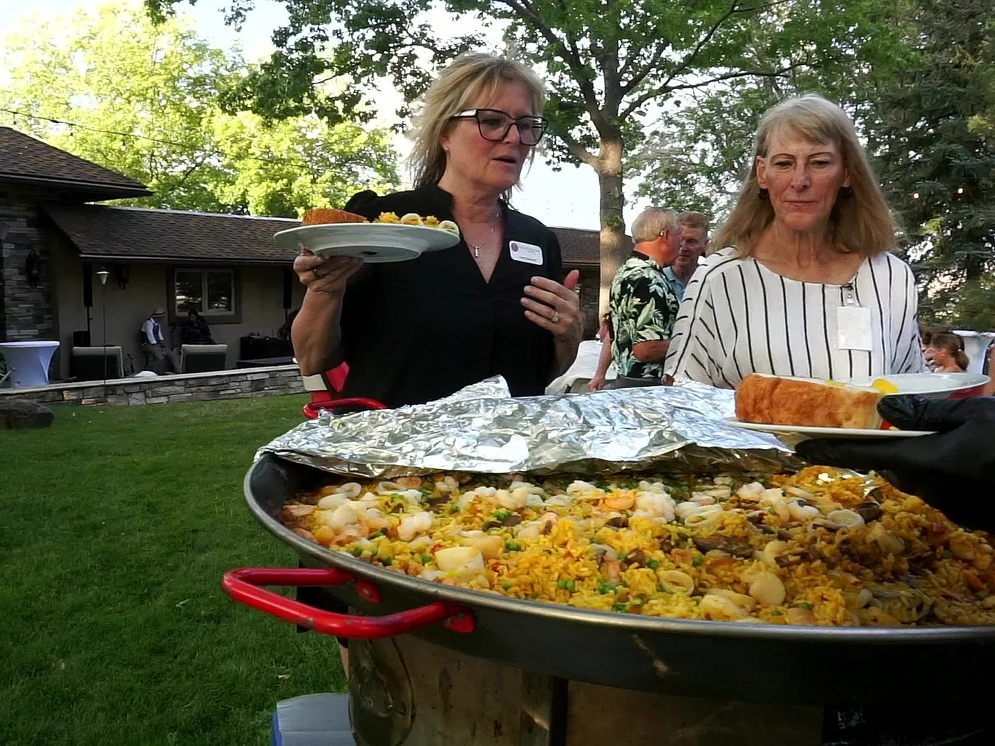 Guests being served paella straight from the pan at an outdoor party