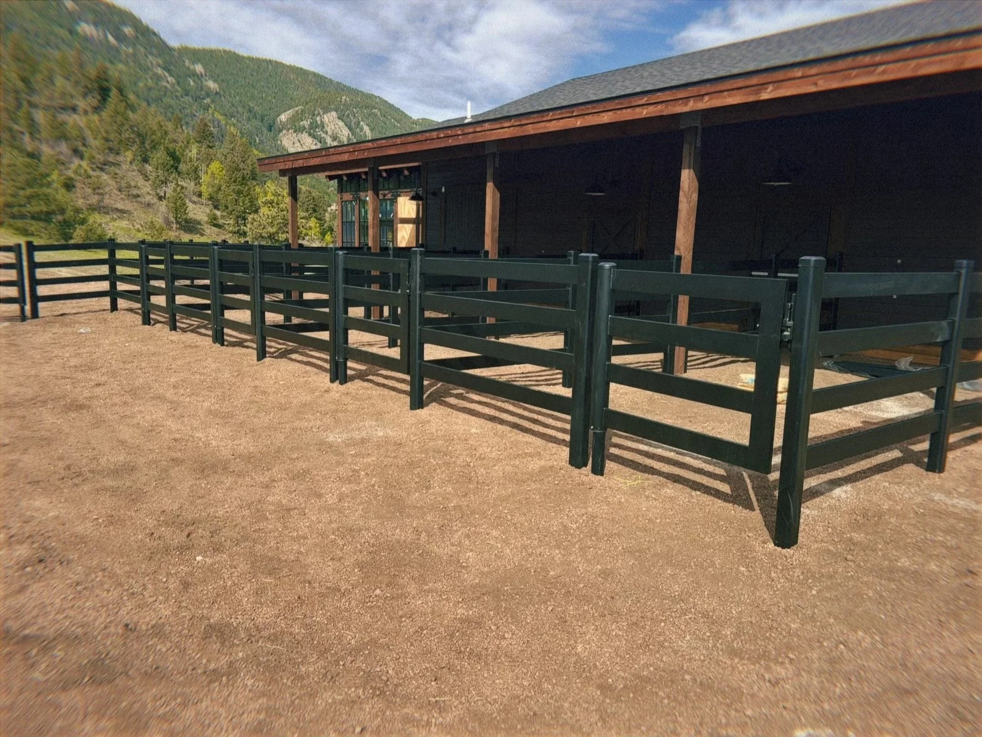 A black wooden outdoor deck or balcony with a railing, overlooking a landscape of green trees, hills, and mountains under a partly cloudy sky. buckly black steel fence

