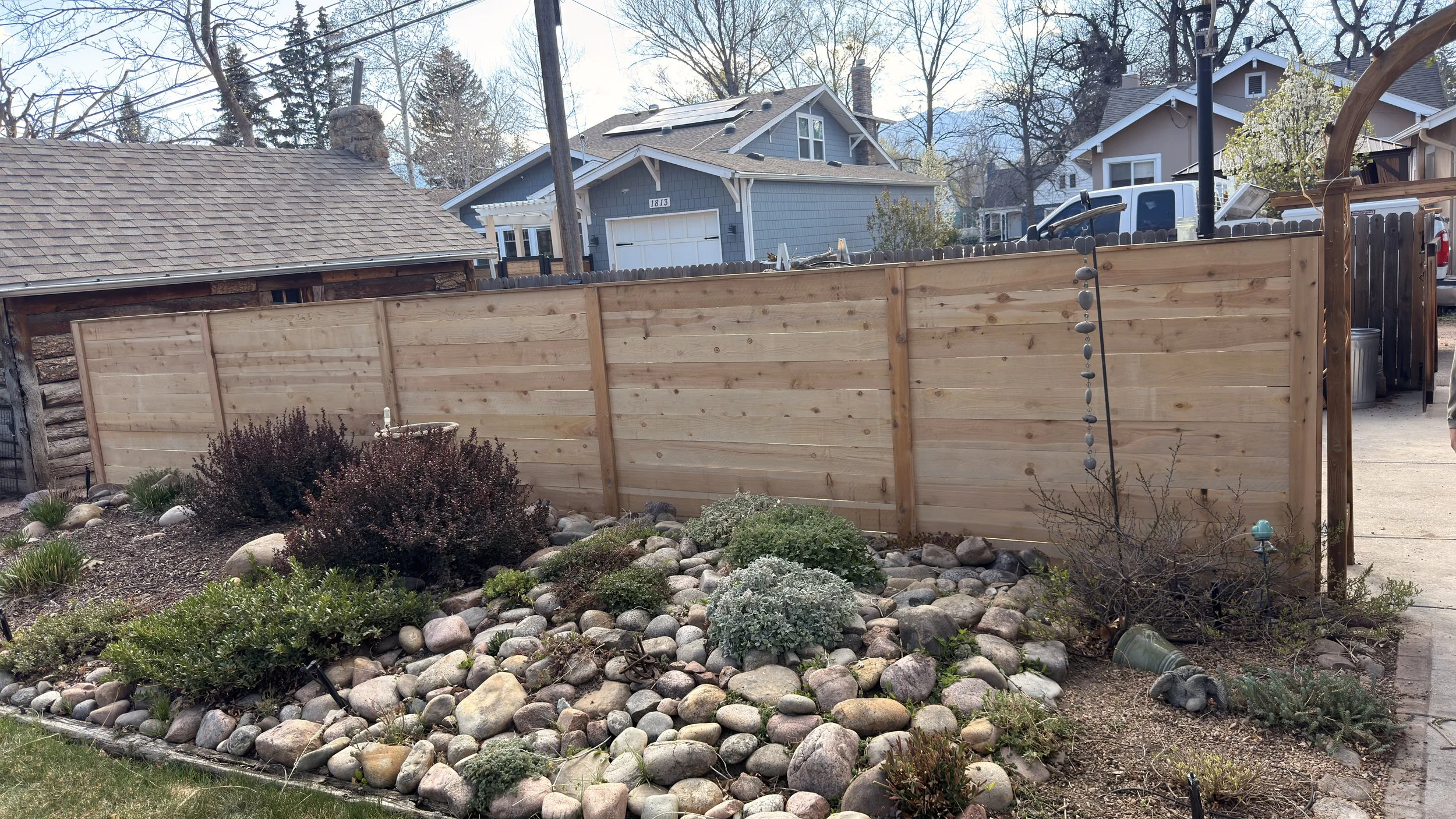 Backyard with a new wood privacy fence, landscaping rocks, shrubs, and neighboring houses in the background.