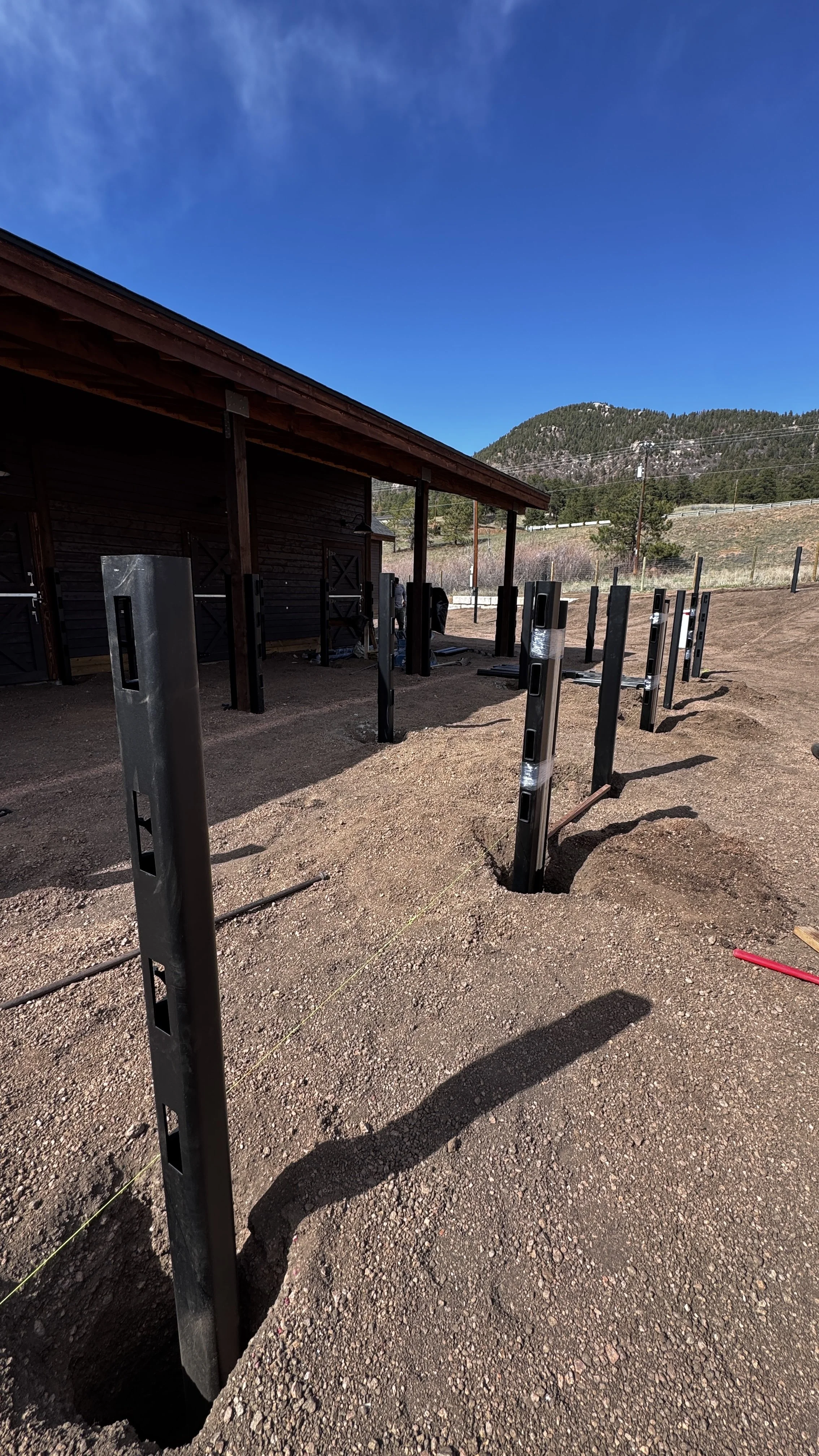 Construction site with metal support beams for a building or structure, under a blue sky in a mountainous area.