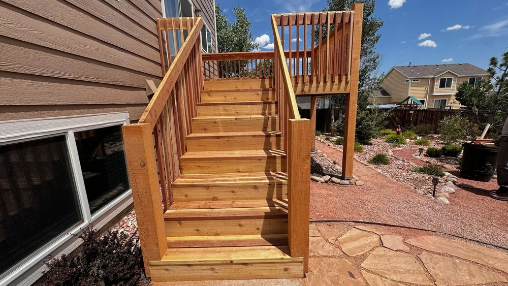 Wood stairs with railing leading up to a deck beside a stone patio