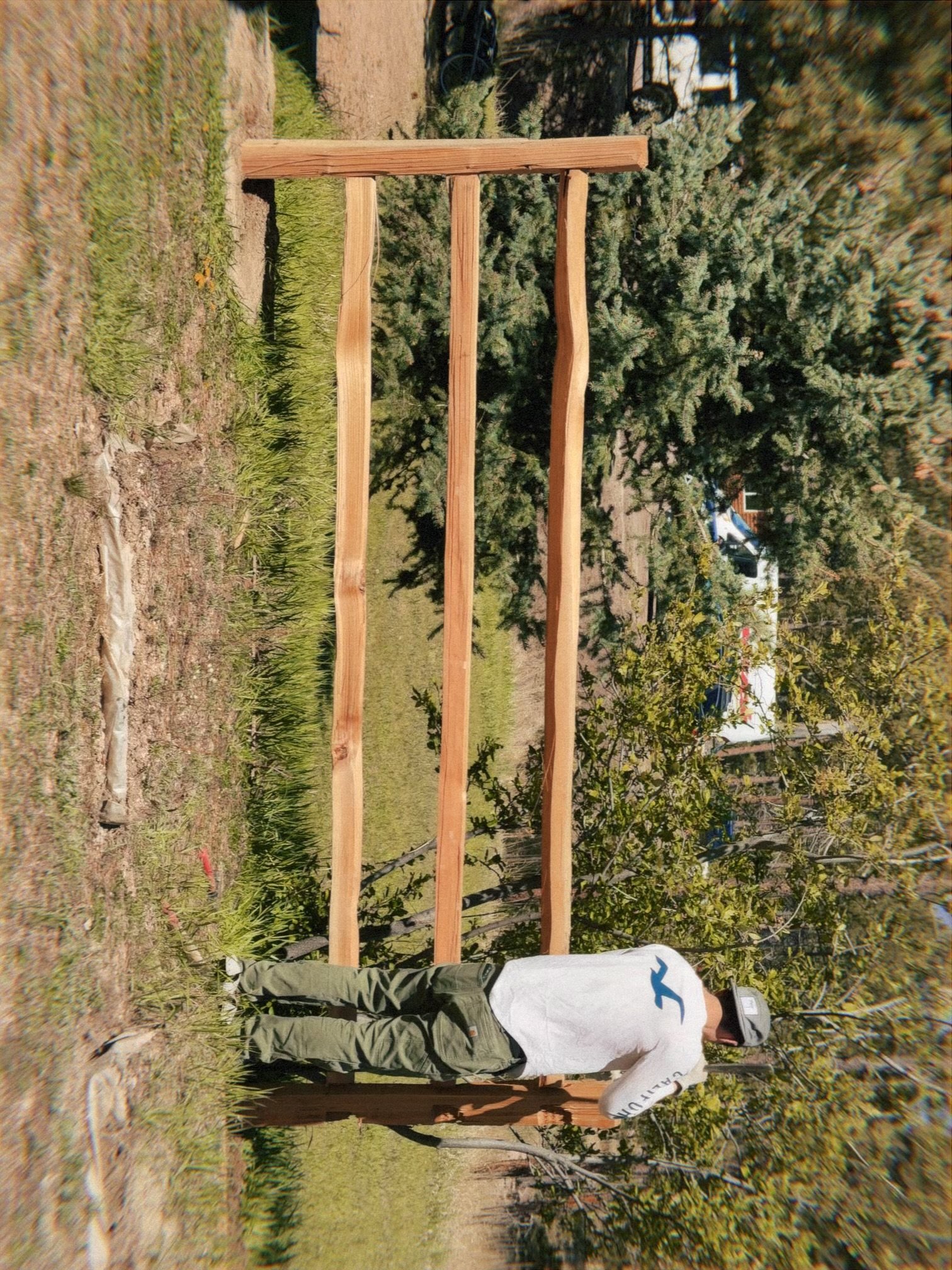 A person building a cedar split rail outdoors, surrounded by trees and grass.