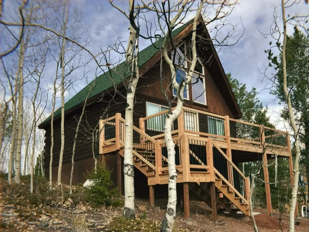 Wood deck with railing, black balusters and stairs on a log cabin among aspen trees