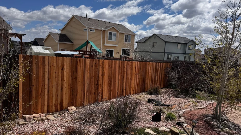 Cedar privacy fence along a backyard with rock landscaping and houses behind