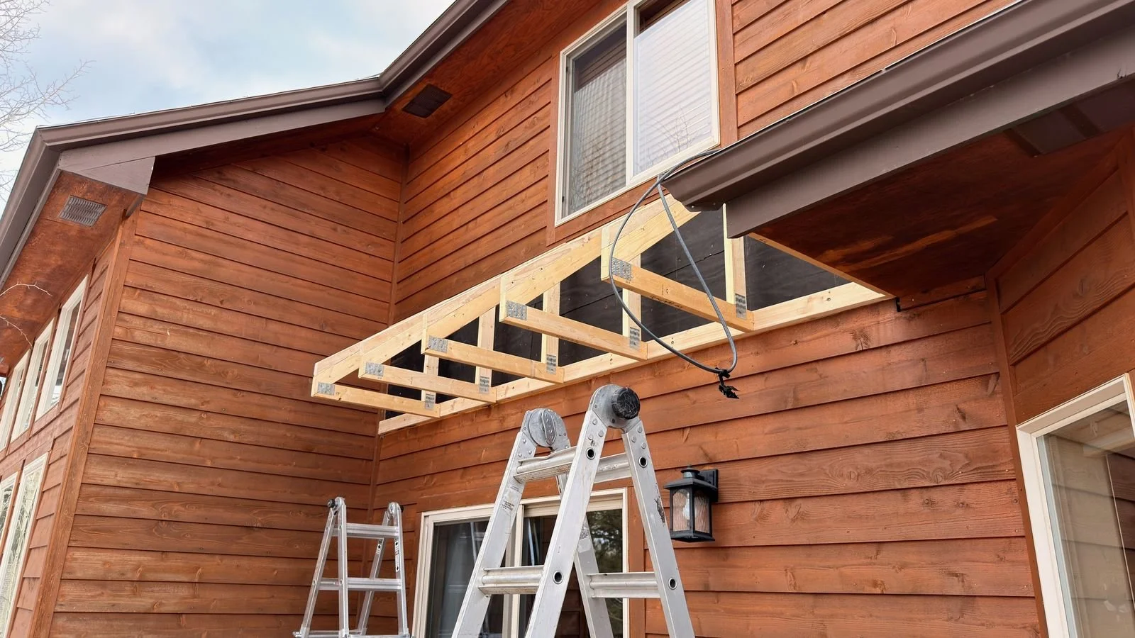 New wood porch roof framing on the side of a cedar-sided house