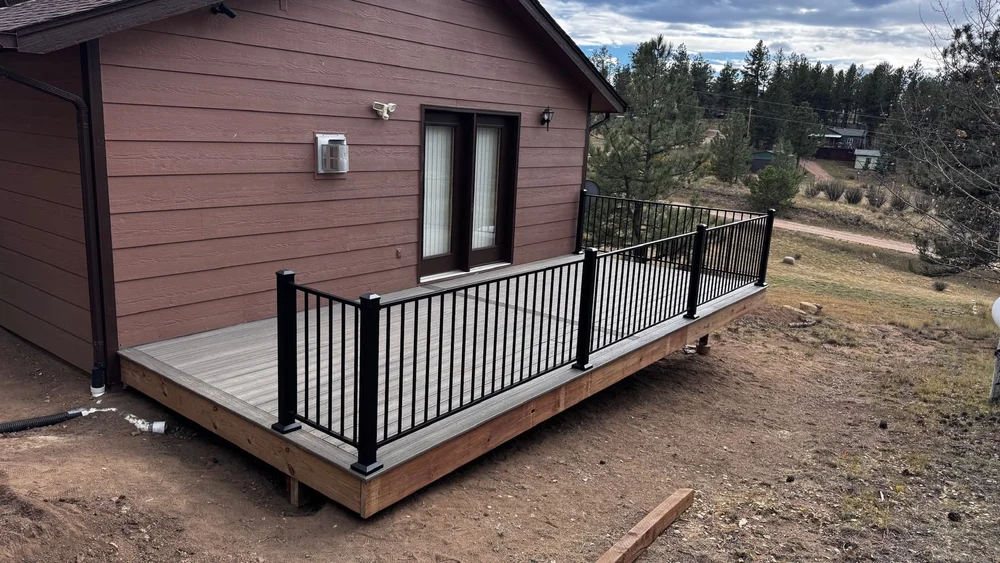 Deck with a black metal railing at the back of a house in the trees
