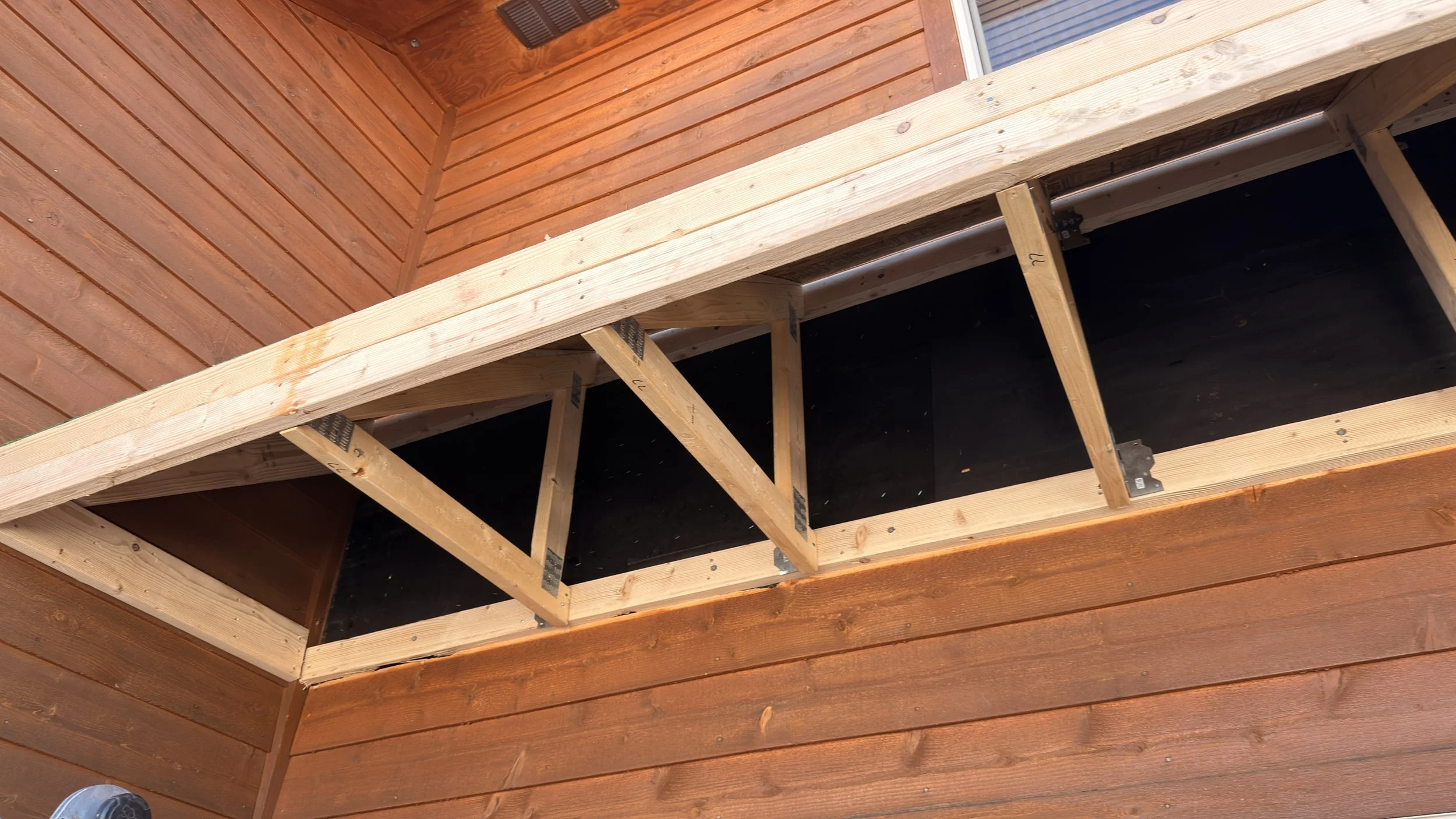 Wooden deck or balcony under construction, showing framing and partially finished surface, attached to a wooden house exterior