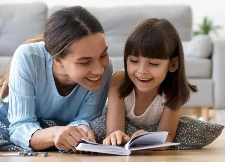 A woman and a girl lying on the floor, looking at a photo album and smiling.