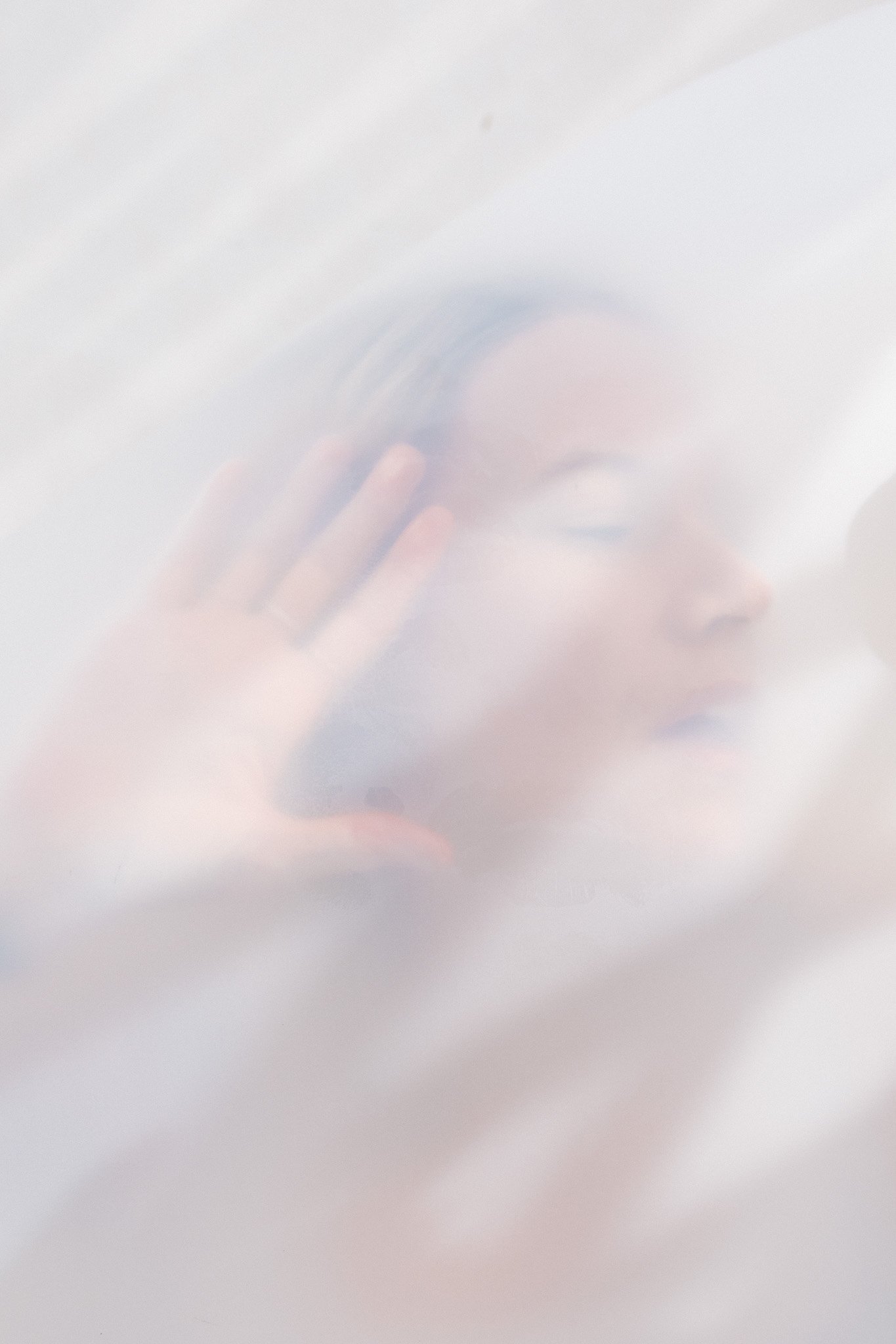 A person taking a photo of their face with a camera or phone in a mirror, partially obscured by bright, hazy lighting.
