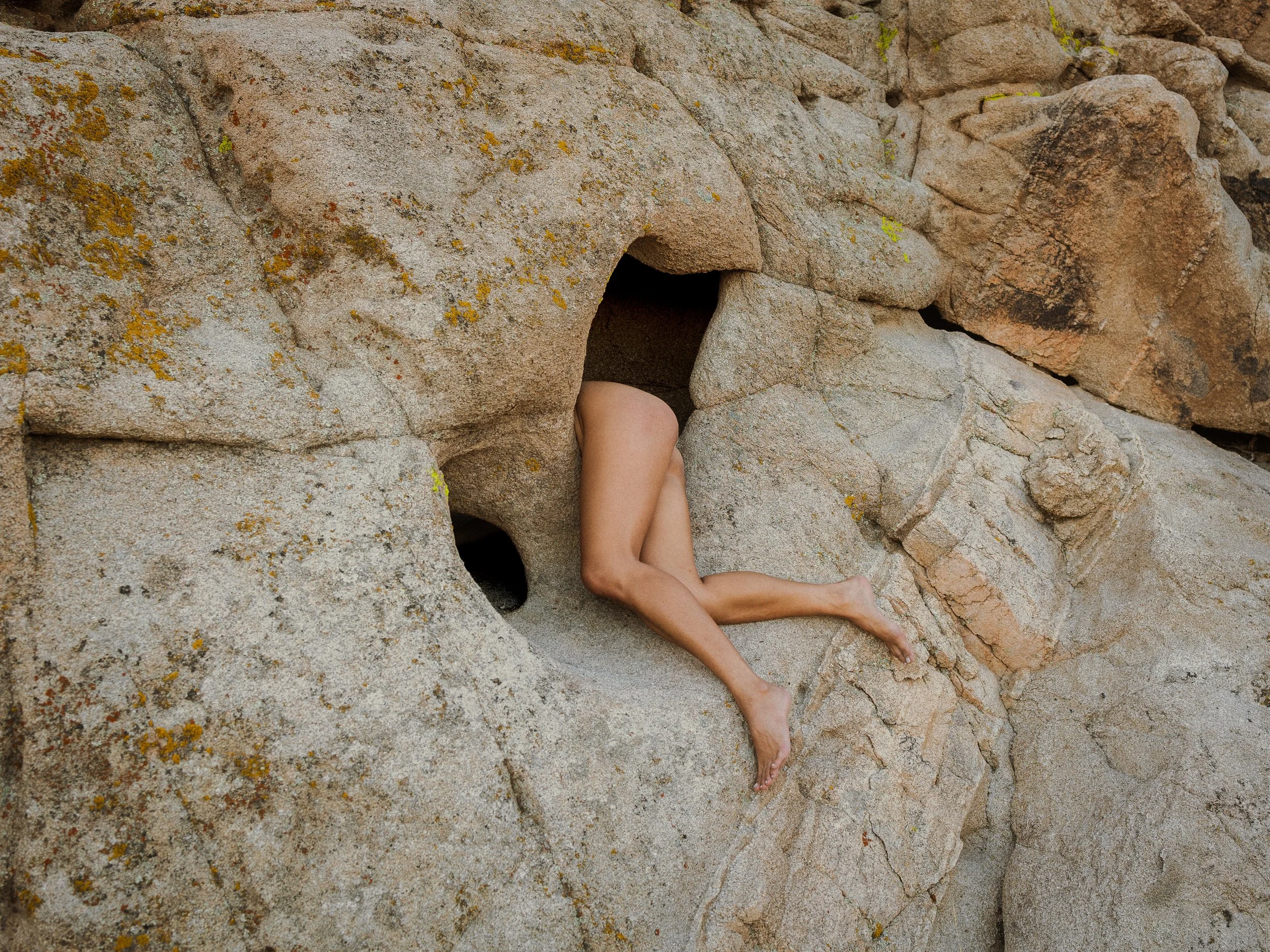 A person with bare legs and arms climbing through a hole in a large rocky formation.