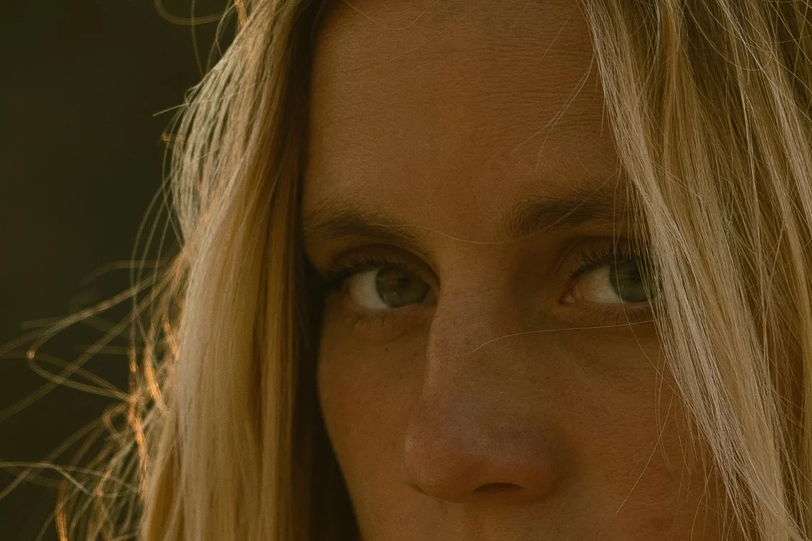 Close-up of a woman with blonde hair and light eyes, looking to the side.