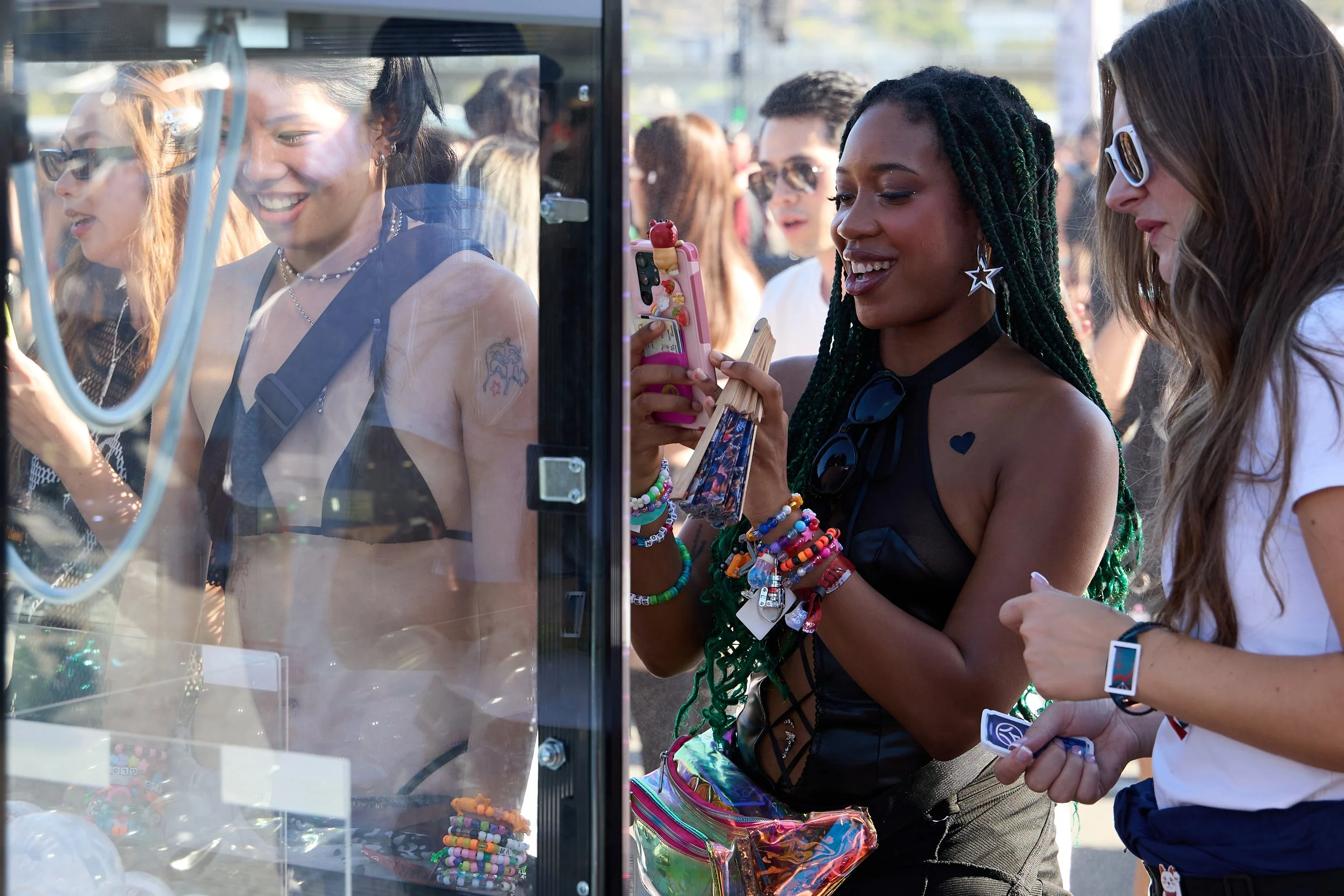 Group of women at an outdoor event looking at a vending machine with small toys and trinkets, some holding smartphones.