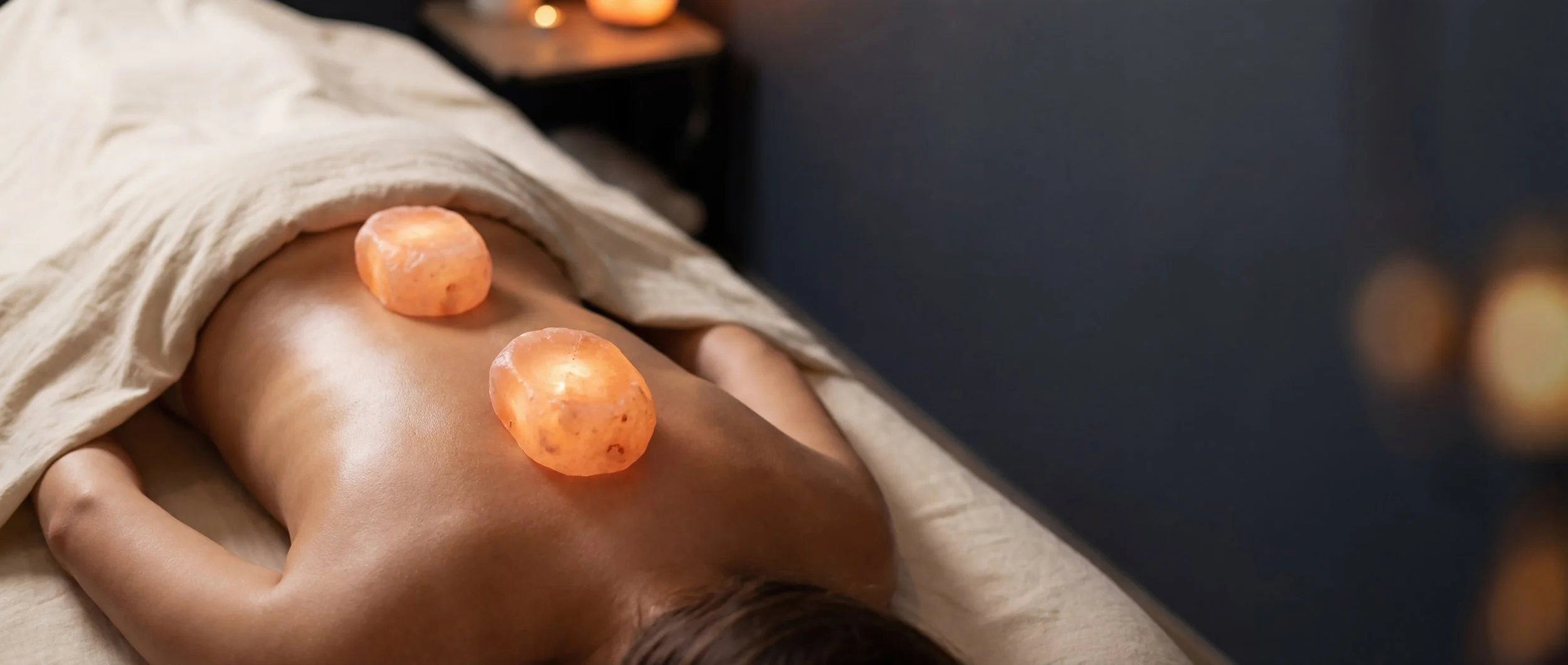 A person lying on a massage table with salt stones placed on their back for a hot stone massage.